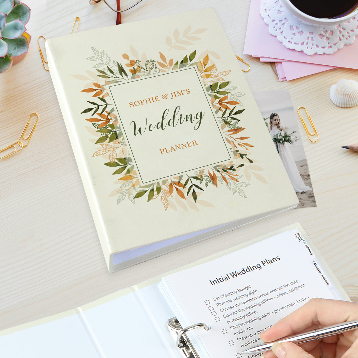 Hand holding a personalised autumnal wedding planner beside an open planner